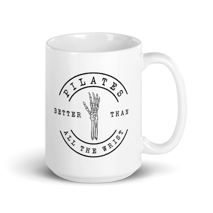 White 15oz mug with handle on the right. The mug says "Pilates Better Than All The Wrist" with a skeleton hand in black text. 