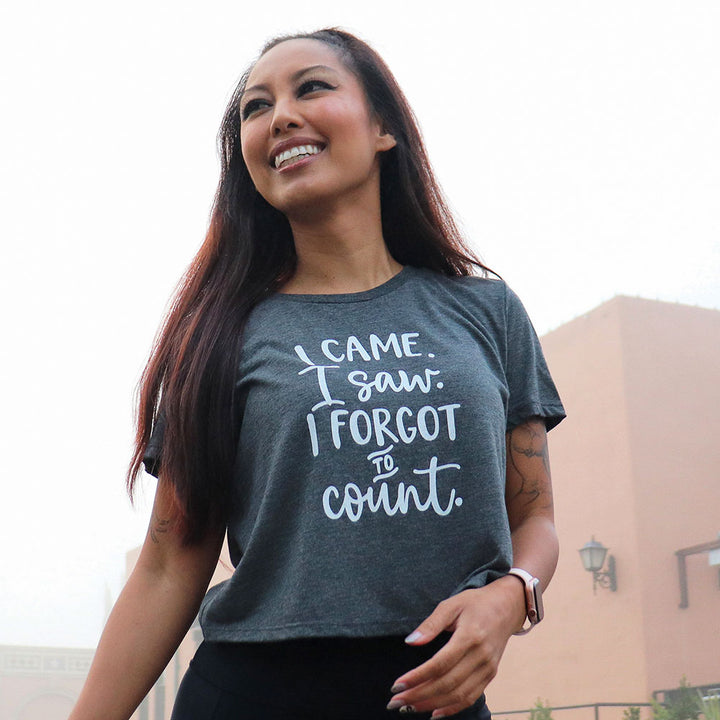 Woman wearing a dark grey cropped women's cut t-shirt that says "I came. I saw. I forgot to count." in white bold text.
