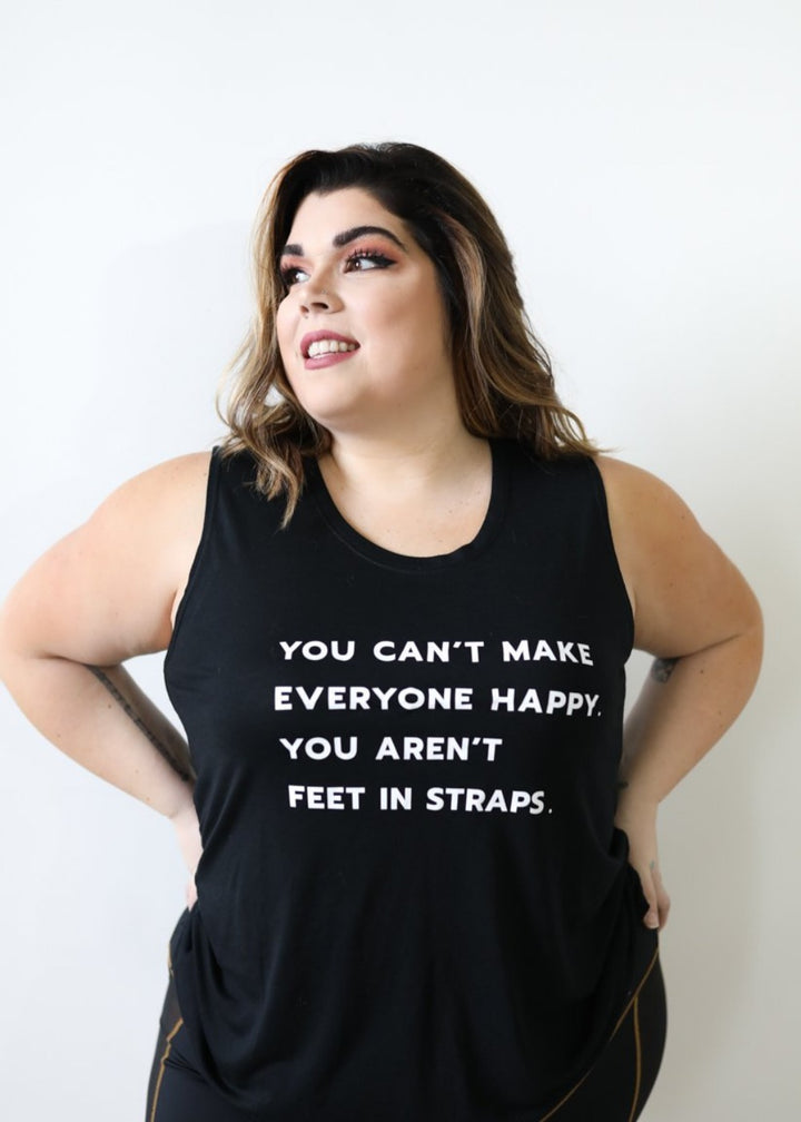 A  woman wearing a black muscle tank top that says "you can't make everyone happy; you aren't feet in straps" in white text on the front